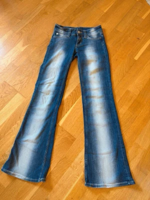 Blå bootcut jeans från cheap Monday/weekday - Säljer ett par blå bootcut jeans med snygga slitningar och ljusa partier framtill och baktill. Jeansen har klassisk femficksmodell, låg midja och dragkedja. Storlek: 24/30