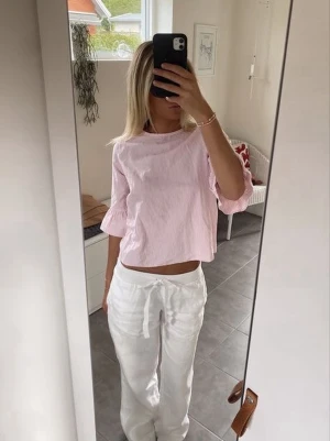 Rosa- och vitrandig blus med volangärm - Söt blus i ljusrosa och vitt med smala ränder och volangdetaljer vid ärmsluten. Modellen är croppad och har trekvartsärm. Perfekt för dig som gillar en feminin och avslappnad stil.