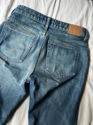 Weekday Jeans - Säljer ett par blå jeans med rak passform och snygg vintage tvätt. Jeansen har klassiska fem fickor, normal midja och kontrastsömmar. Materialet är denim i bomull och de har en läderpatch bak i midjan. Perfekta för en avslappnad och trendig look.
