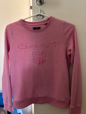 Rosa sweatshirt från GANT - Rosa sweatshirt från GANT med broderad logga och sköld på bröstet. Storlek XS