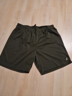 SOC tränings shorts  - Mörkgröna träningsshorts från SOC med elastisk midja och enkel design. Tillverkade i ett lätt och snabbtorkande syntetmaterial, perfekta för sport och aktivitet. Diskret logga på vänster ben.
