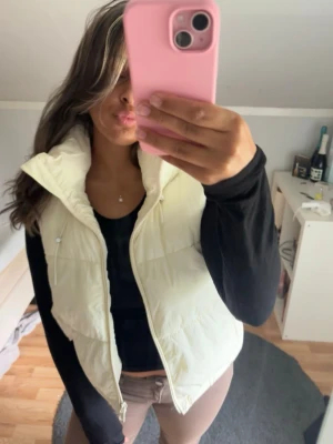 Vit dunväst - Snygg vit dunväst med dragkedja och hög krage. Västen har en huva. Perfekt att slänga över en hoodie eller långärmad tröja för extra värme. Passar till många olika outfits och är riktigt skön att bära. Skavanker på näst sista bilden
