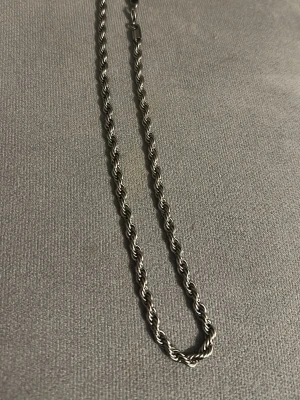 Silverfärgat tvinnat halsband - Säljer ett stilrent halsband i silverfärg med tvinnad kedja Halsbandet har en enkel och klassisk design som passar till många olika stilar Perfekt accessoar för dig som gillar minimalistiska smycken
