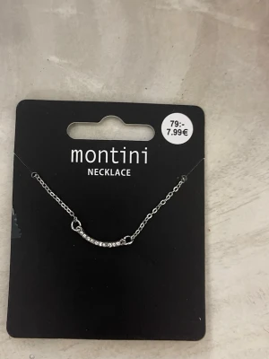 Silverhalsband med stenar från Montini - Snyggt halsband i silverfärg från Montini med en tunn kedja och en böjd stav dekorerad med små gnistrande stenar. Perfekt för att addera lite extra bling till din outfit.
