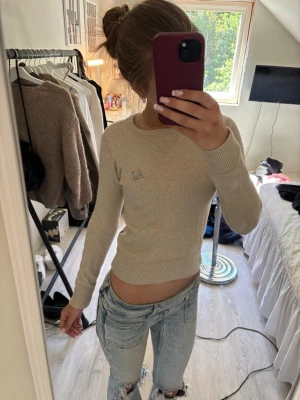 Beige stickad tröja från Armani Jeans - Snygg beige stickad tröja från Armani Jeans med diskret AJ-logga på bröstet. Tröjan har rund halsringning, långa ärmar och ribbade muddar vid ärmslut och nederkant. Perfekt till jeans för en clean och stilren look. Liten över bröstet och lång i armarna, skulle gissa på att den passar som en xxs. 