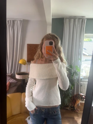 Vit off shoulder stickad tröja - Säljer en vit stickad tröja med bred off shoulder-krage. Tröjan har lång ärm och är gjord i mjukt, stretchigt material. Perfekt för dig som vill ha en enkel men snygg stickad topp till jeans eller kjol.