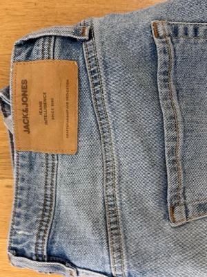 Ljusblå raka jeans Jack & Jones - Säljer ett par ljusblå jeans från Jack & Jones med klassisk femficksmodell och raka ben. Jeansen har en snygg tvättad look och är tillverkade i bomull. Perfekta för en avslappnad och trendig stil.