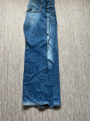 Blå raka jeans med hög midja - Säljer ett par klassiska blå jeans med raka ben och hög midja. Jeansen har en lätt tvättad look med slitningar och normal passform. Perfekta till en avslappnad stil och passar till det mesta. Materialet är denim i bomull.