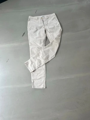Beige chinos med smal passform - Snygga beige chinos med smal passform och klassisk design. Byxorna har framfickor, bälteshällor och stängs med knapp och dragkedja. Perfekta för en clean och stilren look. Materialet känns mjukt och bekvämt.