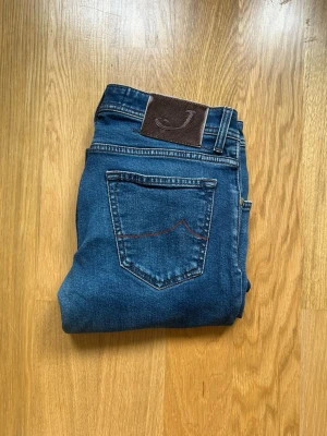 Blåa Jacob Cohen jeans  - Säljer dessa Jacob Cohen jeans. Jeansen har ett litet hål vid gylfen men som lätt går att laga. W:32 Benlängd 103cm  Midja 40cm  Benöppning 16cm