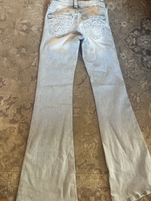 Ljusblå bootcut jeans med broderi - Säljer ett par ljusblå bootcut lågmidjade jeans med tydliga broderade W-detaljer på bakfickorna. Jeasen är från Gina Young och aldrig använd eftersom jag inte gillade hur den satt på mig. 