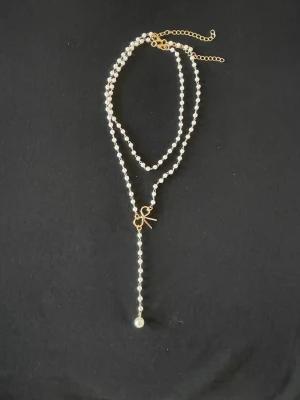 Boho Pärlhalsband i 2 delar - Boho, Snyggt dubbelradigt halsband med vita pärlor och guldfärgade detaljer. Halsbandet har en liten rosett i metall och en längre hängande rad med pärlor som avslutas med en större pärla. Justerbart med kedja i nacken. Perfekt för dig som gillar en söt och trendig stil.  Längd 42+7cm, korta delen 33+7cm