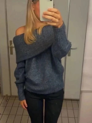 Blå off shoulder stickad tröja - Trendig blå stickad tröja med off shoulder-design och bred krage. Tröjan har en avslappnad passform, långa ärmar och ribbstickade muddar. Perfekt för dig som vill ha en snygg och bekväm look till vardags.