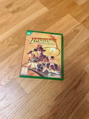 Indiana Jones and the Great Circle Xbox - Xbox Series X-spel Indiana Jones and the Great Circle i original grön plastfodral. Omslaget har äventyrstema med Indiana Jones och flera karaktärer. Spelet är PEGI 16 och innehåller både skiva och kontrollguide. Perfekt för dig som gillar action och äventyr.