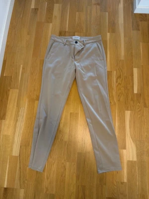 Beige chinos tygbyxor W32 L32 slim  - Snygga beige chinos tygbyxor i klassisk rak modell. Byxorna har två sidofickor, bälteshällor och stängs med knapp och dragkedja. Tillverkade i mjukt bomullsmaterial med lite stretch för extra komfort. Perfekta för en clean och stilren look.