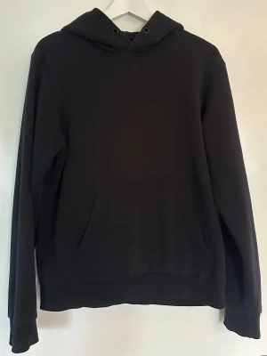 Svart hoodie från Jack & Jones - En klassisk svart hoodie från Jack & Jones med huva och känguruficka framtill. Hoodien har ribbade muddar vid ärmslut och nederkant. Perfekt för en chill och avslappnad stil. Materialet känns mjukt och bekvämt.