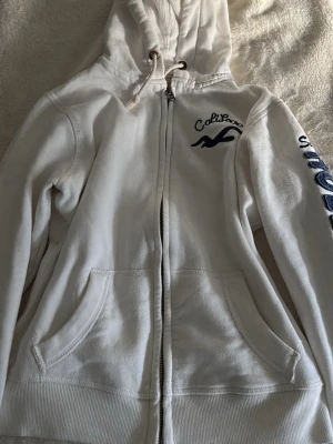Vit zip-hoodie från Hollister - Vit hoodie med dragkedja från Hollister, i storlek S!! Priset kan diskuteras. Skriv om fler bilder eller frågor.