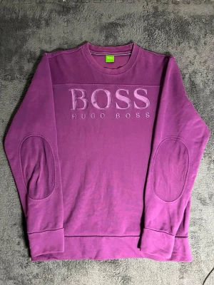 BOSS Hugo Boss – Purple Sweatshirt (L) - Stylish Hugo Boss sweatshirt in a stunning purple shade. Size L, length 70 cm, pit-to-pit 55 cm – comfortable and modern fit. The front features a large BOSS HUGO BOSS embroidery, giving it a premium and distinctive look.  ✅ Condition: Excellent – no wear, no stains 💯 Authenticity: 100% genuine Hugo Boss garment 📦 Shipping: Dispatched immediately after purchase – fast and reliable delivery!  This sweatshirt combines Hugo Boss’s classic style with comfort.