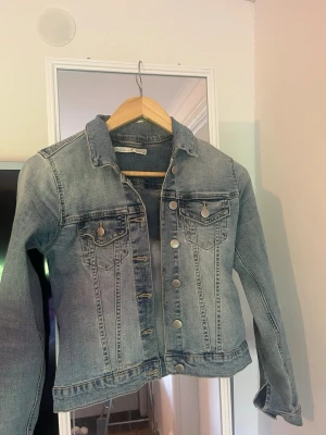 Ljusblå klassisk jeansjacka - Snygg ljusblå jeansjacka med raka sömmar och silverfärgade knappar. Två bröstfickor med lock och knapp, samt klassisk krage. Jackan har en tidlös passform och är tillverkad i slitstarkt denimtyg.