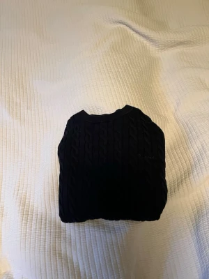 Mörkblå kabelstickad tröja Bondelid - Snygg mörkblå kabelstickad tröja med rund hals och klassiskt flätmönster. Perfekt för dig som gillar en stilren och tidlös look. Tröjan har en mjuk och bekväm känsla och passar till många olika outfits. 