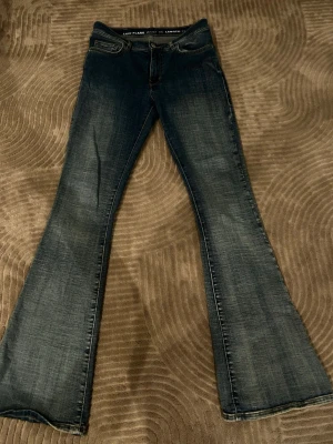 Mörkblå low flare  jeans med utsvängda ben - Snygga mörkblå low flare  jeans med tydligt utsvängda ben och klassisk femficksmodell. Jeansen har en tvättad look med ljusare partier och är tillverkade i denim. Storlek waist xs length 32