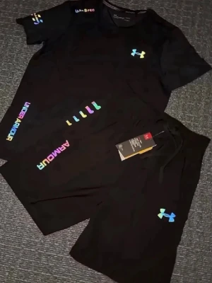 Svart träningsset från Under Armour - Snyggt svart träningsset från Under Armour med t-shirt och shorts. Setet har färgglada loggor och textdetaljer i regnbågsfärger. Perfekt för gymmet eller löpning. Materialet är lätt och andas, vilket gör det bekvämt under träning.