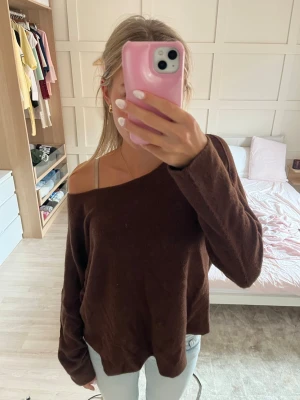 Brun off shoulder stickad tröja - Mysig brun stickad tröja från Moretti Milano i off shoulder-modell. Tröjan har en avslappnad passform och långa ärmar, perfekt för lager på lager. Materialet känns mjukt och skönt mot huden. Enkel att styla med jeans eller kjol.