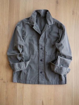 Olivgrön overshirt med knappar - Stilren olivgrön overshirt i bomull med klassisk krage och knäppning framtill. Långa ärmar med uppvikta muddar och en bröstficka. Perfekt lager-på-lager-plagg för en avslappnad look.