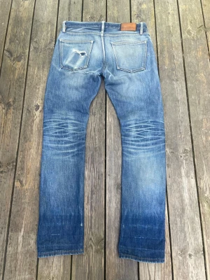 Blå slitna jeans med raka ben - Säljer ett par blå jeans med raka ben och slitna detaljer på både fram- och baksida. Jeansen har klassisk femficksdesign och en ljus tvätt med tydliga slitningar och hål för en avslappnad look. Perfekta för dig som gillar en casual och trendig stil. W 41cm L 105cm