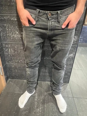  Replay Jenas  - Snygga grå slim fit jeans från Replay med klassisk femficksdesign och diskreta slitningar. Jeansen har en något tvättad look och tydliga sömmar, samt Replay-logga vid fickan. Perfekta för en trendig och avslappnad stil.