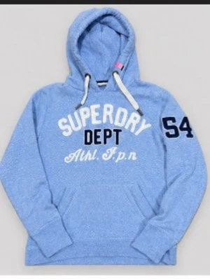 Blå Superdry hoodie med tryck - Ljusblå hoodie från Superdry med vit och marinblå text på bröstet och siffran 54 på ärmen. Klassisk huva med vita snören och känguruficka framtill. Mjuk och skön bomullsblandning, perfekt för en avslappnad stil.