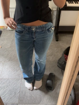 Blå bootcut jeans med låg midja - Säljer ett par blå bootcut jeans med låg midja och klassiska fem fickor. Jeansen har ljus tvätt och vita sömmar som ger en snygg kontrast. Perfekta för en avslappnad och trendig look. Storlek 158
