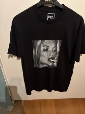 Svart t-shirt med tryck Print in Black - Cool svart t-shirt från Print in Black med ett stort svartvitt tryck av ett ansikte på framsidan. Klassisk passform och rund hals. Perfekt för dig som gillar streetwear och grafiska motiv.