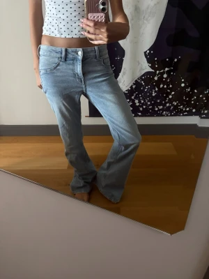Ljusblå bootcut jeans - Säljer ett par ljusblå bootcut jeans med klassisk femficksdesign och normal midja. Jeansen har en avslappnad passform över låren och utsvängda ben. Perfekta för en trendig och avslappnad look.