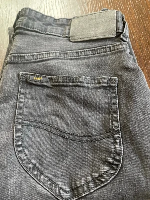 Svarta jeans från Lee med smal passform. Riktigt schyssta. Passar någon som har 150cm - Snygga svarta jeans från Lee med klassisk femficksdesign och smal passform. Jeansen har en diskret logga på bakfickan och är tillverkade i mjukt denimtyg. Perfekta för dig som gillar en stilren och enkel look.