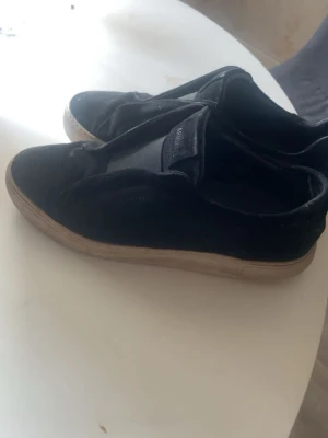 Svarta sneakers från Axel Arigato - Stilrena svarta sneakers från Axel Arigato med låg profil och vit sula. Ovandelen är i mocka.  utan synliga snören och passar perfekt till allt. Skick 7/10