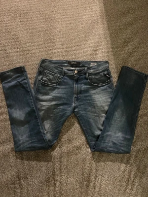 Replay Anbass - Säljer ett par blå jeans från Replay i modellen anbass med snygga tvättade detaljer. Klassisk femficksmodell med Replay-logga på myntfickan och metallknapp i midjan. Perfekta för dig som gillar en modern och avslappnad stil. Storlek W32 L32