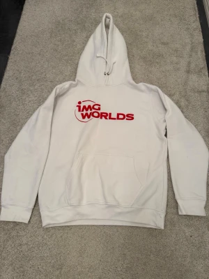 Vit IMG Worlds Hoodie med tryck (Stl M) - Skön vit hoodie med rött tryck fram och siffra bak. Merch från IMG Worlds. Perfekt som en stilren hoodie till vardags eller chill! 