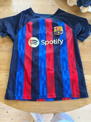 Barcelona matchtröja blå/röd - Säljer en FC Barcelona matchtröja i blått och rött med klubbmärke och Spotify-logga på bröstet. Tröjan har korta ärmar och är tillverkad i ett lätt, snabbtorkande material som passar perfekt till fotbollsträning eller match.