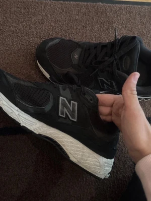 Svarta New Balance sneakers - Snygga svarta sneakers från New Balance med vit sula och meshdetaljer. Skorna har en klassisk låg siluett och reflekterande N-logga på sidan. Perfekta för dig som gillar sportig och stilren look.