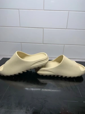 Beige chunky tofflor med räfflad sula - Säljer ett par beige tofflor med chunky design och kraftigt räfflad sula. Tillverkade i ett mjukt och flexibelt material som ger skön komfort. Perfekta för att glida runt hemma eller på språng. Minimalistisk look utan synliga loggor.
