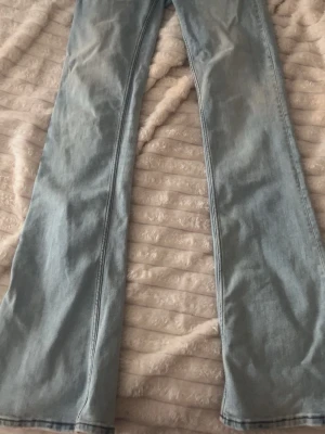 Ljusblå bootcut jeans - Säljer ett par ljusblå bootcut jeans med klassisk femficksdesign och markerade sömmar. Jeansen har en grön patch bak i midjan och är tillverkade i ett mjukt denimtyg. Perfekta för en avslappnad och trendig look.