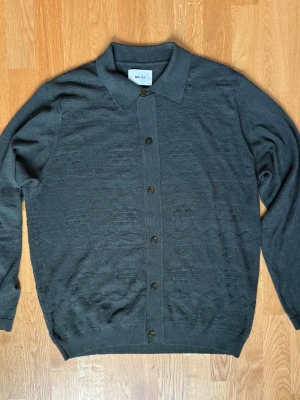 Mörkgrön cardigan från NN07 - Stilren mörkgrön cardigan med knäppning framtill från NN07. Tröjan har ett diskret mönster i stickningen och perfekt för lager-på-lager. Storleken på tröjan är i XL och har använts lätt