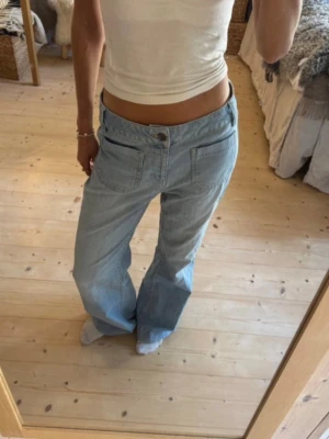 Ljusblåa vida jeans med fickor - Säljer ett par ljusblå jeans med breda ben och stora framfickor. Jeansen har låg midja och en avslappnad passform som ger en cool och trendig look. Perfekta för dig som gillar en casual och bekväm stil. Materialet är klassisk denim i bomull.
