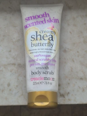 Treaclemoon Shea Butterfly Body Scrub - Creamy body scrub med sheasmör och naturliga skrubbkorn. Doft av söt blomma, 100% vegansk och dermatologiskt testad. Perfekt för att exfoliera huden före brun utan sol eller rakning. Tuben rymmer 225 ml och har guldfärgat lock.
