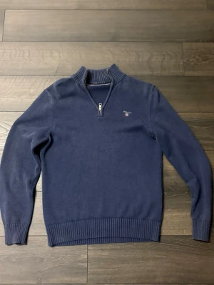 Mörkblå stickad tröja med dragkedja - Blå stickad quarterzip tröja ifrån GANT. Fungerar perfekt med en skjorta under om man vill vara uppklädd eller som ett vardagligt plagg.                             St:S 