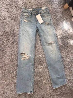 Zara Ljusblåa raka slitna jeans - Trendiga ljusblå jeans med raka ben och flera slitningar på låren och knäna. Jeansen har klassisk femficksmodell och är tillverkade i denim. Perfekta för en avslappnad och cool stil.