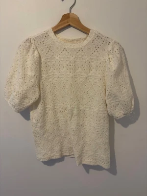 Vit spetsblus med puffärm - Säljer en söt vit blus i spets med puffiga korta ärmar och rund halsringning. Blusen har ett detaljerat spetsmönster över hela plagget och ger en romantisk vibe. Perfekt att styla med jeans eller kjol för en trendig look.