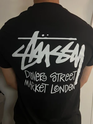 Stussy Dover Street Market T-shirt svart - Snygg svart Stussy T-shirt med klassiskt Dover Street Market London-tryck. Stilren design framtill och stort Stussy-tryck på ryggen. Perfekt för streetwear och en enkel, stilren outfit.  Mycket fint skick, sparsamt använd. Svart färg. Se bilder för skick och detaljer.