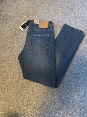Jack & Jones jeans  - Snygga blå jeans från Jack & Jones med klassisk femficksdesign och läderpatch bak i midjan. Jeansen har raka ben och är tillverkade i ett mjukt denimtyg med lätt stretch. Perfekta för en avslappnad och trendig look.
